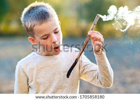 Child boy playing with smoking wooden stick outdoors.
