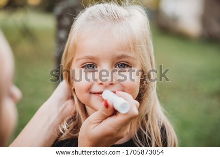 cute blond girl outside with dry chapped lisp, mum putting lip balm on a child 