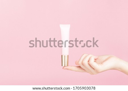 Unbranded flacon on female finger. Plastic tube for cream,body lotion, toiletry. Container for professional cosmetics product. Skincare and beauty concept. Mockup, copy space. Isolated on pink. Royalty-Free Stock Photo #1705903078