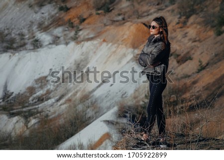 Beautiful young girl on the shore of a pond, dressed in black pants and a leather jacket
