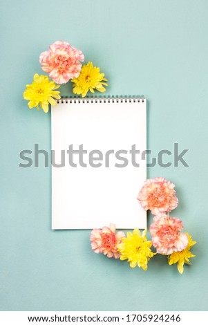 Mockup blank notebook with pink and yellow flowers and on a turquoise canvas background. Top view, flat lay with copy space