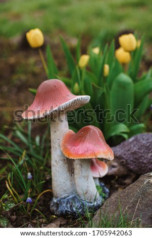 
Handmade yellow tulips with a toy mushroom are used to decorate the garden on a cloudy spring day
