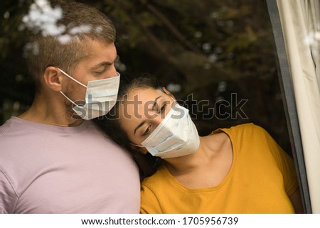 Young couple wearing face mask in front of the window and cuddling each other at home. Coronavirus and Quarantine concept Royalty-Free Stock Photo #1705956739