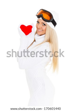 Young woman in winter clothes and ski glasses holds in hands a red heart on a white background.