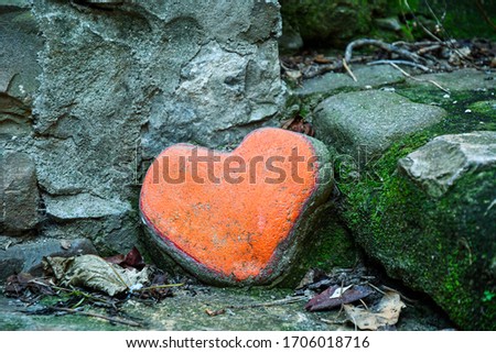 Close-up of a heart-shaped red painted stone in the corner of a gray stone alley, Italy