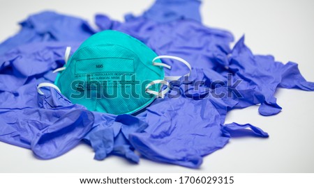 A turquoise N95 particulate respirator and surgical mask on top of many medical gloves. Royalty-Free Stock Photo #1706029315