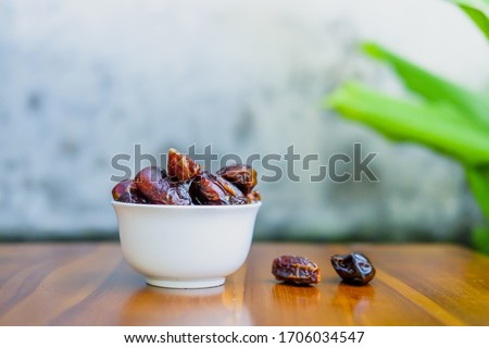Bowl white with delicious dried dates (Kurma) isolated on wooden board brown. Royalty-Free Stock Photo #1706034547