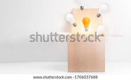 White and orange energy-saving light bulbs flying out of the open carton box on white background. Be different, out of the box thinking concept.  