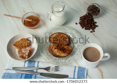 Delicious homemade breakfast. French toast with sweet golden honey, a mug of coffee with milk, a linen napkin and cutlery close-up on a pastel green marble background. Selective focus.