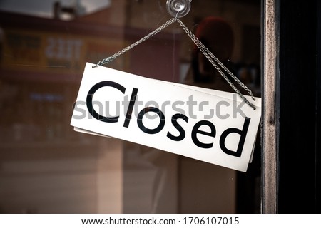 Classic black and white sign and chain hangs on an angle in a glass storefront or door due to the shop or retail business being closed during the COVID-19 outbreak and government stay at home orders.