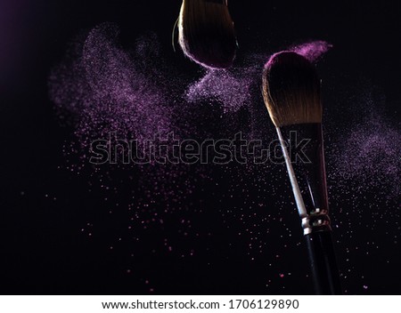 Art of visage.  Closeup photo of two professional black make-up brushes with purple  powder isolated on black background with copy place. 