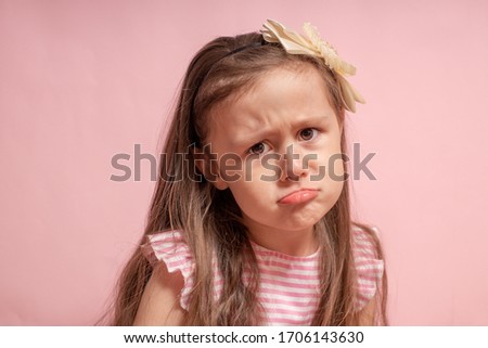 The little girl on a pink background was offended by folding her arms and frowning eyebrows