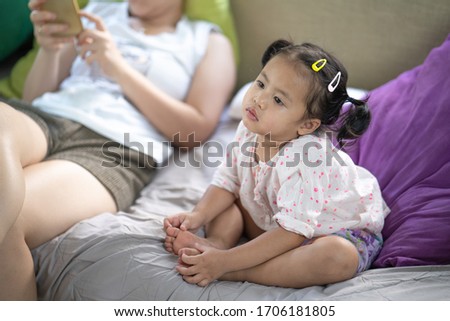 Cute little girl sitting with her mother at the couch watching television during Covid 19 quarantine. 