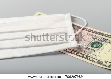 White medical mask and money on a gray background close-up. The problem of purchasing and high cost of medical masks.