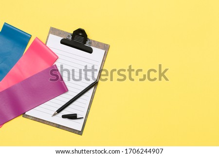  Expanders for fitness and elastic bands for sports and an open Notepad with a pen on a yellow background. The concept of drawing up a training plan