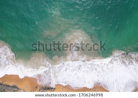 aerial drone bird view shot of the sea shore with turquoise blue water, large white waves and foam, empty beach with yellow sand, black rocks forming beautiful textures, patterns, shapes. Sri Lanka