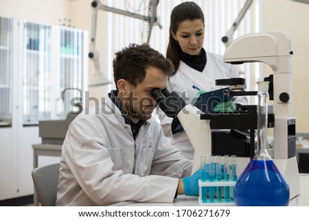 Workflow of two chemists in the laboratory. The senior chemist examines the test sample under a microscope, and his assistant takes notes. Scientific activity. The creation of a vaccine. Royalty-Free Stock Photo #1706271679