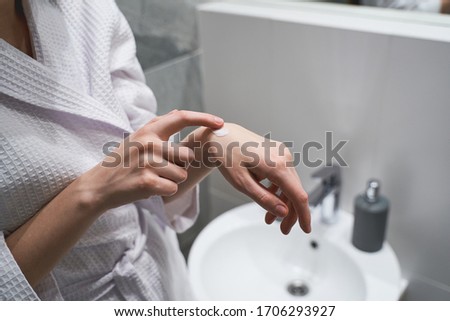 Cropped photo of a girl in a waffle bathrobe rubbing a cream to her skin