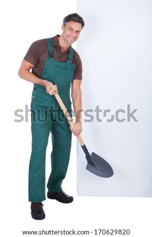 Portrait Of Cheerful Male Gardener With Shovel Presenting Blank Placard