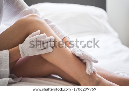 Cropped photo of a young woman in a waffle bathrobe doing dry brushing in bed