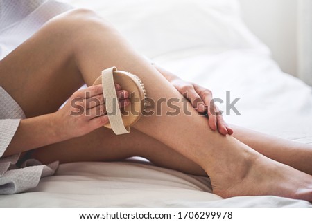 Cropped photo of a young Caucasian woman doing lymphatic drainage with a bath body brush