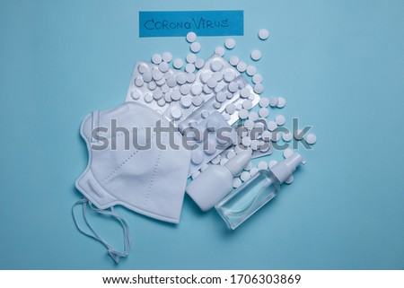 sanitizer, medical face mask and pills on a blue background