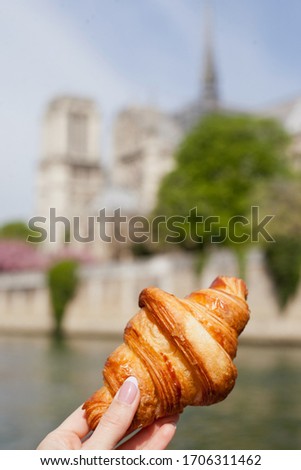 A croissant in a hand of a woman with Notre Dame de Paris on the background