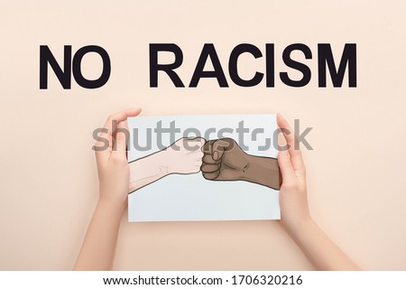 cropped view of woman holding picture with drawn multiethnic hands doing fist bump near no racism lettering on beige background Royalty-Free Stock Photo #1706320216