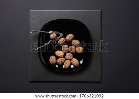 a fantastic still-life studio image of wallnuts on a black plate & nutcracker on black dark background, topview
