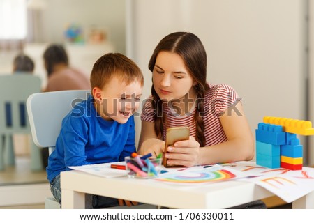 Motherhood concept. Brunette and son play with plastic building blocks. mom show somethimg funny in phone. Excited preschooler playing with his smiling mother or kindergarten teacher. Royalty-Free Stock Photo #1706330011