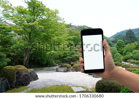 human hand is holding phone for taking picture with red blur maple leave  background