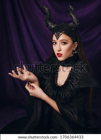 Stock Photo - Maleficent demonic. Girl dressed as a fairy witch in raincoat and with horns