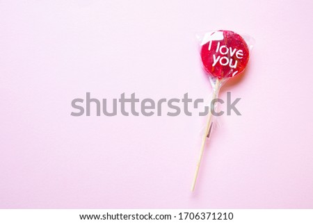 a sweet wrapped "I Love you" red lollypop against a pastel yellow background, flat lay, top view, minimalistic