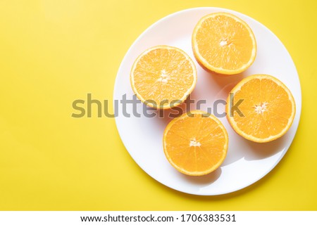 a fantastic minimal photograph of four fresh slices of oranges on a white plate on a yellow background