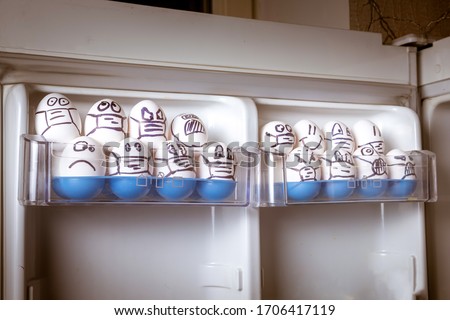 quarantine easter concept. close up of diverse chicken easter eggs with doodle emotional faces wearing medical masks crowding in fridge door