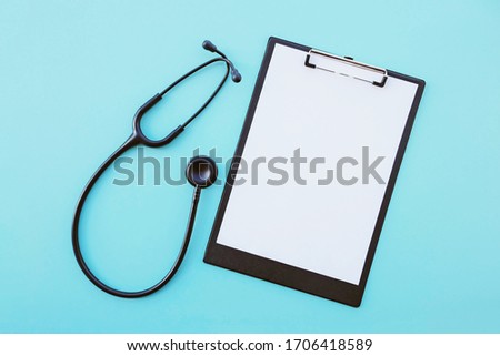 Black modern stethoscope and blank medical form on light blue background. Medicine and healthcare, cardiology, medical education. Acoustic medical device. Space for text. Flat-lay, top view.