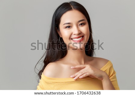 Close up young happy attractive Asian woman wearing yellow showing shoulder dress with sweet smile face isolated on grey background.