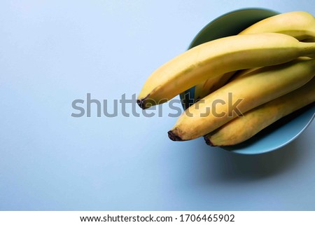 a fresh view of a bunch of bananas resting in a light blue food bowl with a pastel light blue background, top view