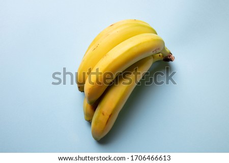 a fresh view of a bunch of yellow bananas resting on a pastel light blue background, top view