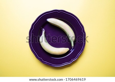 a fantastic pastel coloured image of two bananas an a decorative purple plate with yellow background, flat lay, top view