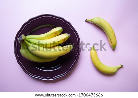 a stylish pastel coloured image of a bunch of bananas an a decorative purple plate with pink background, flat lay, top view