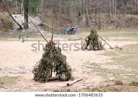Two tepees built with twigs and branches of conifers standing on sandy ground in the forest with bicycles in the background Seen in Germany in April. Royalty-Free Stock Photo #1706483635