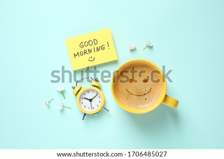 Delicious coffee, alarm clock and card with GOOD MORNING wish on light blue background, flat lay