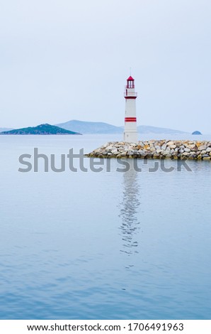Lighthouse on a stone road in the middle of calm sea with views of mountains and fog.