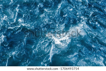 Deep blue stormy ocean water with splashes and foam, top view. Natural background photo texture with soft focus