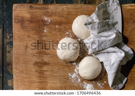 Dough for pizza cooking. Three balls of fresh homemade wheat dough under linen cloth on wooden table. Home baking. Flat lay, space