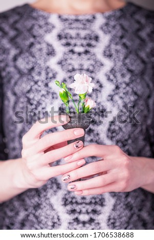 Female hands holding pale pink carnation flowers in black waffle cone on a black and white dress. Snake skin texture