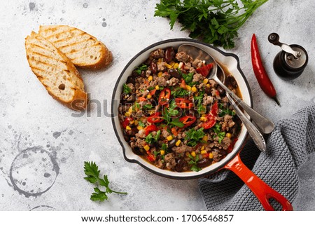 Traditional Mexican food - Chili con carne with minced meat and vegetables stew in tomato sauce in a cast iron pan on light gray slate or concrete background. Top view with copy space.