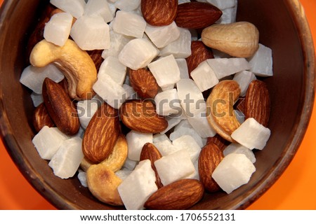 Cashew nuts, almonds and coconut in a mug on an orange background