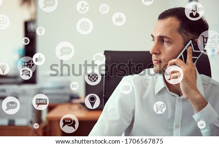 Closeup portrait of a young man working with a phone with a laptop holding a mouse in his hands. Around icons with cloud technology, internet, thumbs up, digital marketing, GPS, IT, social network